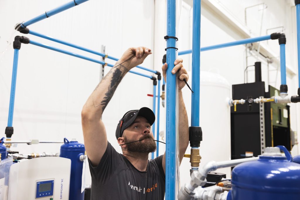 Bearded worker in a cap tightens a blue PVC pipe in an industrial plumbing setup