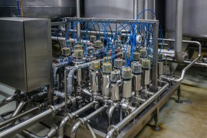 Row of stainless steel vessels and pipes with blue electrical cables in an industrial processing setup.