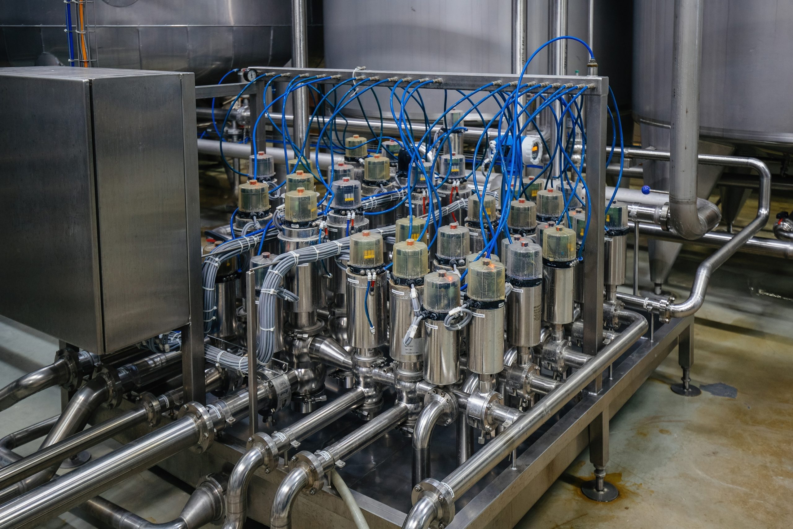 Row of stainless steel vessels and pipes with blue electrical cables in an industrial processing setup.